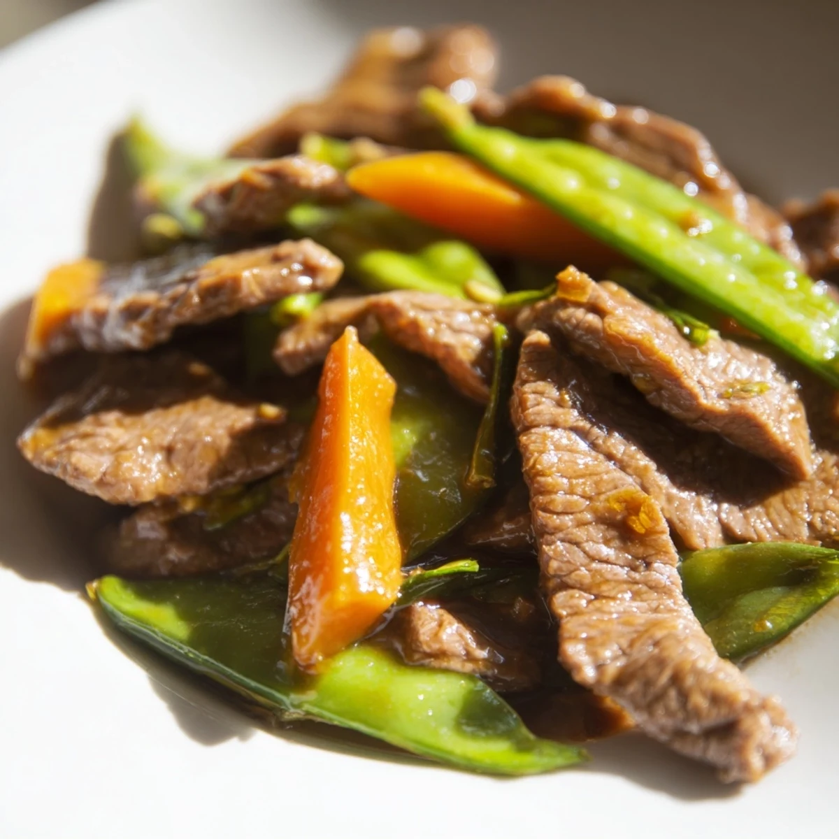Golden-brown beef strips glisten in a skillet, mingling with vibrant snap peas and orange carrot matchsticks in a glossy, savory sauce.  