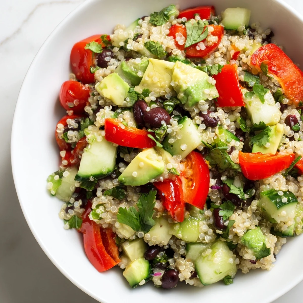 Fluffy quinoa salad with black beans, crisp veggies, and lime dressing, served in a white bowl.