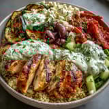 A vibrant, finished Healthy Grilled Mediterranean Bowl topped with juicy halloumi, cherry tomatoes, olives, and a drizzle of creamy tzatziki sauce.