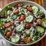 Freshly prepared Mediterranean Green Salad Bowl featuring crunchy cucumbers, briny Kalamata olives, and vibrant red onion on a bed of greens.  