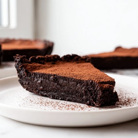 A close-up view of the Decadent Dark Chocolate Brownie Tart, showcasing its glossy, fudgy filling in a golden-brown crust, dusted with cocoa powder.