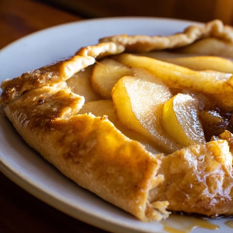 A close-up of a golden, flaky Rustic Pear and Ginger Galette with tender, spiced pear slices and a bubbly filling on parchment paper.