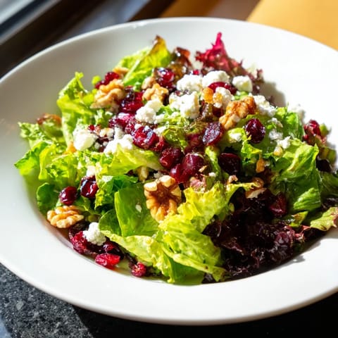 Seasonal Cranberry and Walnut Celebration Salad served on a white platter, featuring sliced apples, red onion, and crumbled goat cheese for a festive holiday side.