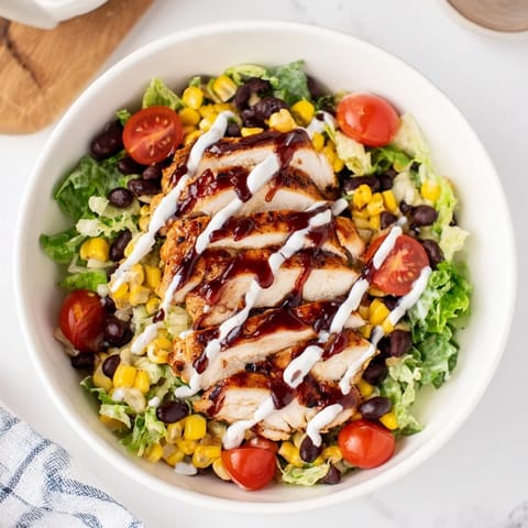 Vibrant BBQ Chicken Salad with juicy chicken, fresh tomatoes, red onion, and avocado, served on a rustic wooden table.