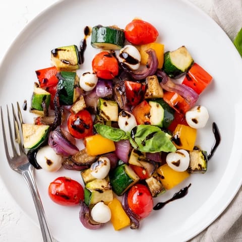 Roasted Veggie Caprese Salad with caramelized vegetables and mozzarella pearls drizzled with sweet balsamic glaze on a white serving platter.