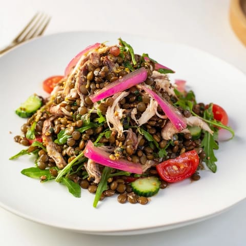 Freshly tossed Lentil & Chicken Spring Salad with tender lentils, juicy chicken, peppery arugula, and vibrant pickled onions on a plate.