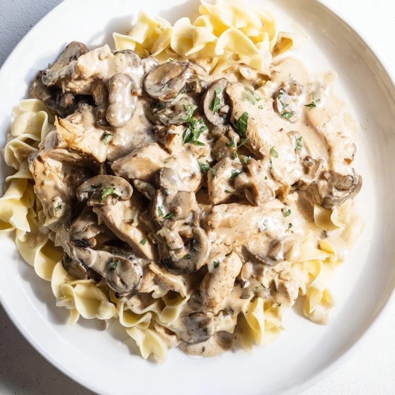 A close-up of Chicken and Mushroom Stroganoff highlights the glossy sauce clinging to noodles and tender chicken pieces.