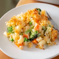 A serving of Garden Veg Mac and Cheese with golden baked cheese and visible peas, broccoli, and carrots.